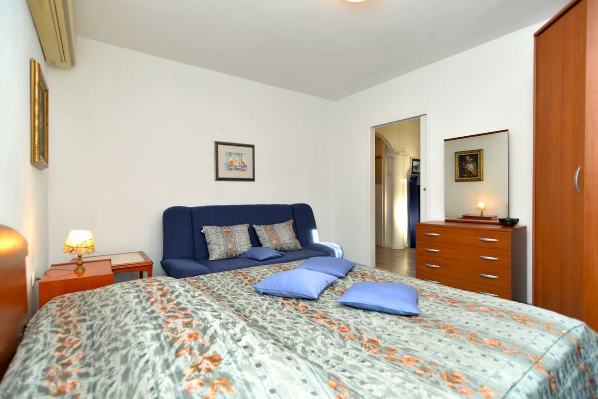 Quarto com cama, penteadeira, mesa de cabeceira, abajur e um quadro na parede.