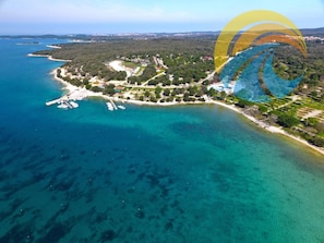 An aerial view of a coastal area with a marina, clear blue waters, and a mix of residential and natural landscapes. - Rooms Milan 1370 (Rovinj)