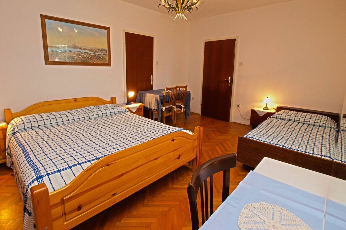 Une pièce avec deux lits en bois, une table à manger avec des chaises, un lustre et un tableau au mur.