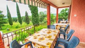 A covered outdoor seating area with tables and chairs, a view of a green landscape with trees, and a brick wall. - Rooms Milan 1370 (Rovinj)