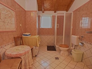 A bathroom with a toilet, sink, and shower. There is a table with a towel and a chair. - Rooms Milan 1370 (Rovinj)