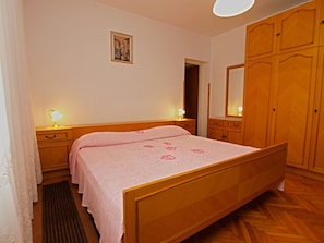 A bedroom with a wooden bed, two bedside tables with lamps, a wooden wardrobe, and a framed picture on the wall.