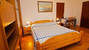 A bedroom with a wooden bed, a nightstand with a lamp, a chair, a table with a tablecloth, and a painting on the wall. - Rooms Milan 1370 (Rovinj)
