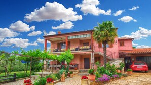 A two-story pink villa with a balcony, a stone courtyard, and a red car parked in front. - Rooms Milan 1370 (Rovinj)