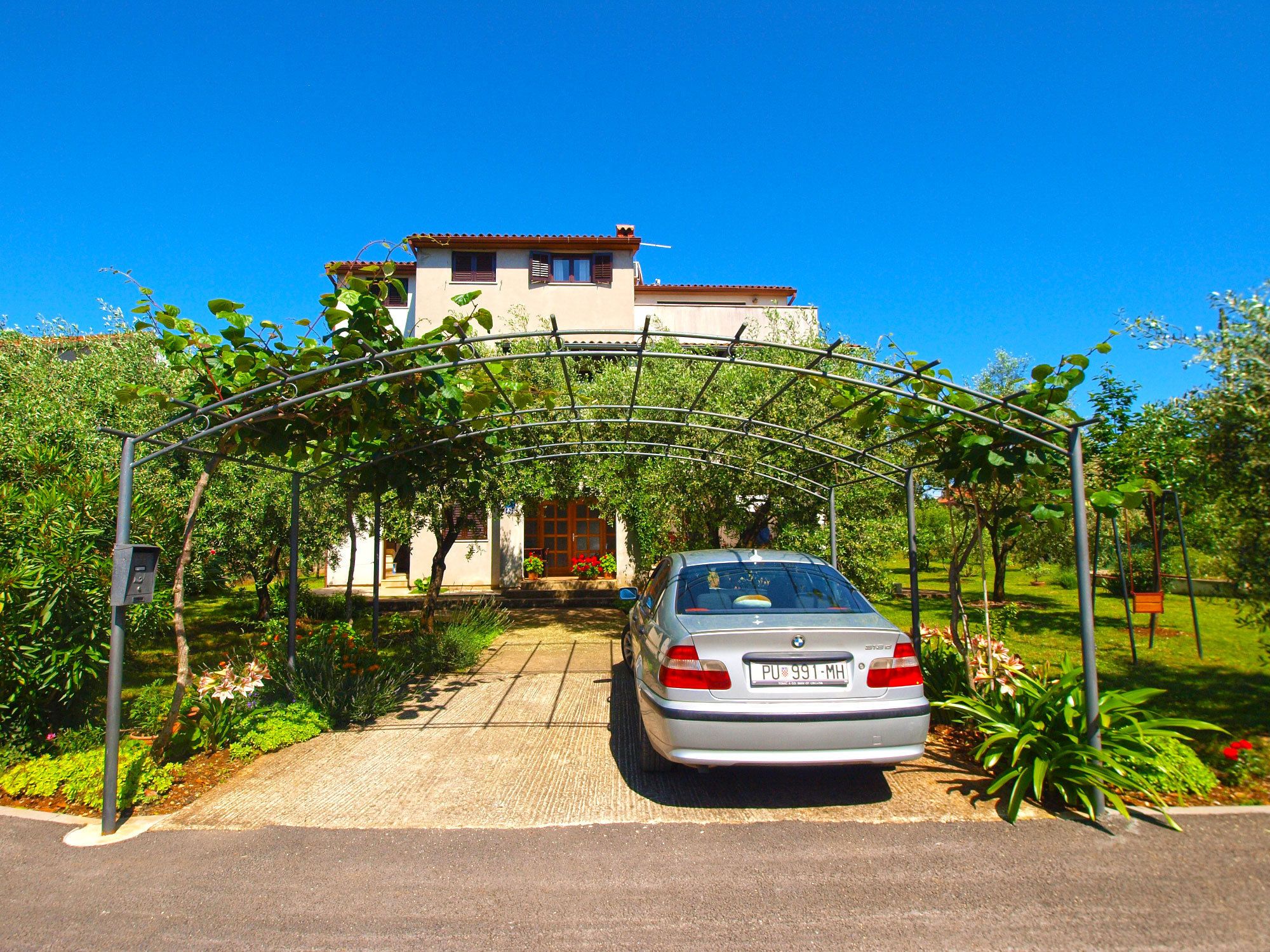 A car parked under a metal archway leading to a house with a tiled roof.