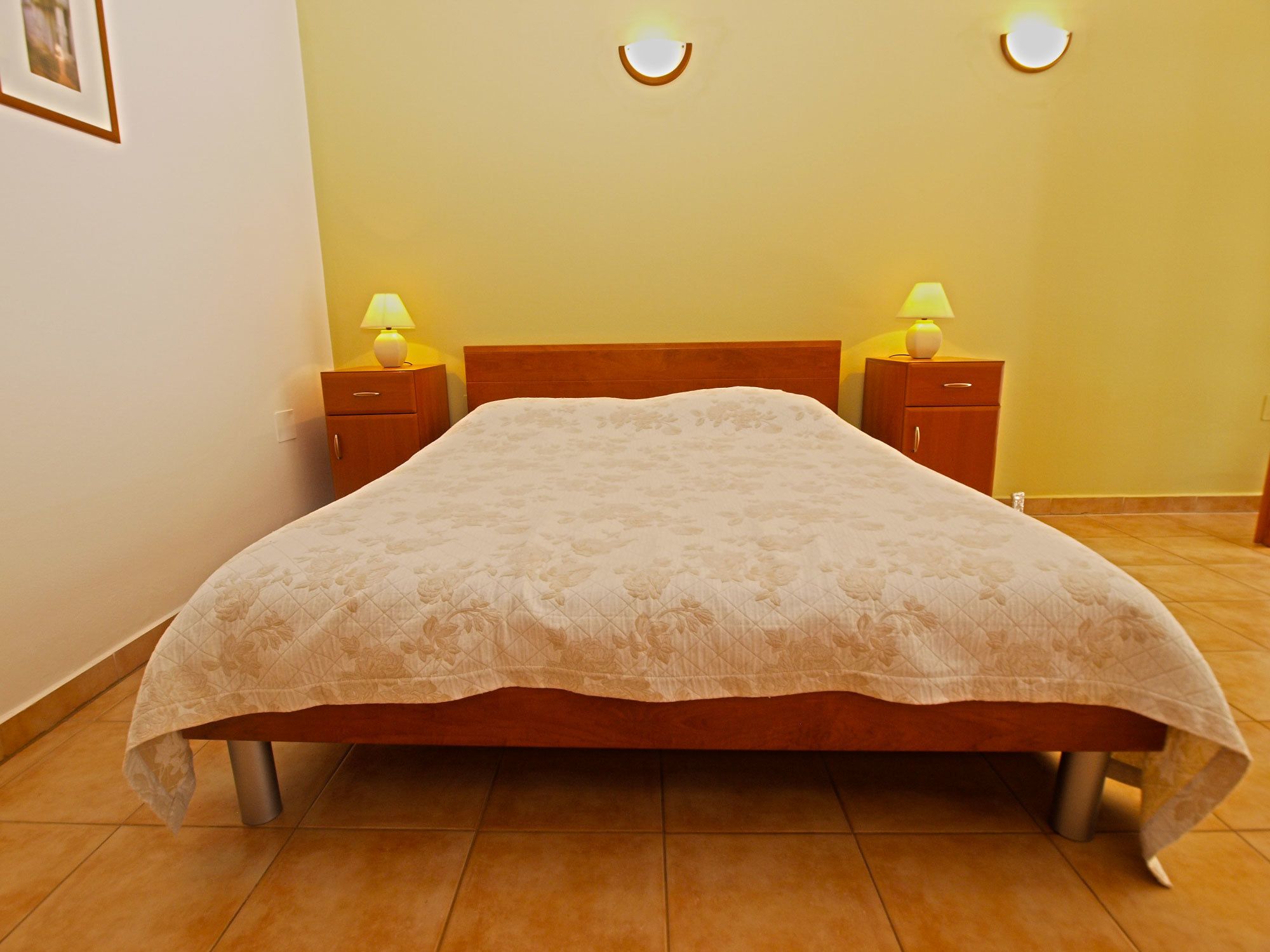 A neatly made bed with a floral bedspread, two bedside tables with lamps, and a wall-mounted light fixture.