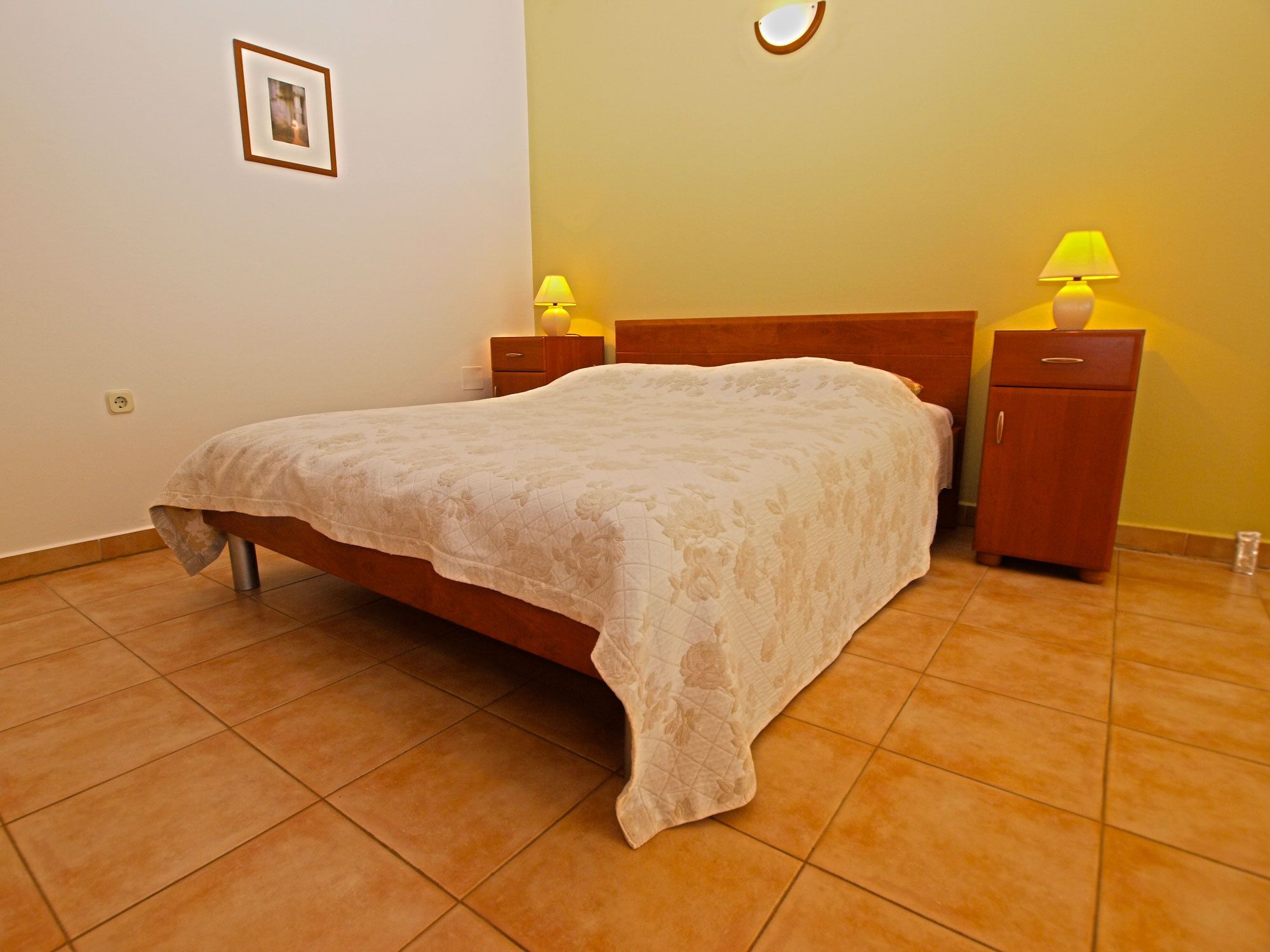 A neatly made bed in a room with a wooden headboard, two bedside tables with lamps, and a small cabinet.