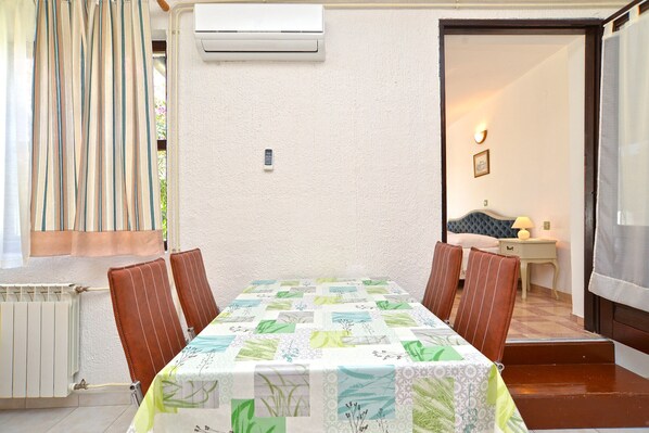 A dining area with a table covered by a floral tablecloth, surrounded by four chairs. An air conditioning unit is mounted on the wall above the table.