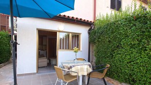A patio with a table and chairs, a blue umbrella, and a small window with a view of the interior. - Apartments Elsa 534 (Pula)