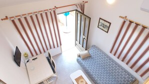 A compact room with a bed, a desk, and a chair. There is a window with curtains, a framed picture on the wall, and a small table with a vase of flowers. - Apartments Elsa 534 (Pula)