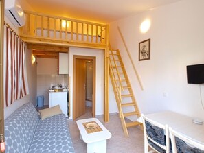 Un espacio habitable compacto con un entrepiso para dormir, kitchenette y un sofá.