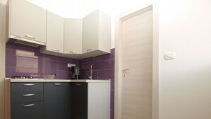 A compact kitchen with dark cabinets, a coffee maker, and purple-tiled backsplash. - Apartments Orijana 898 (Pula)