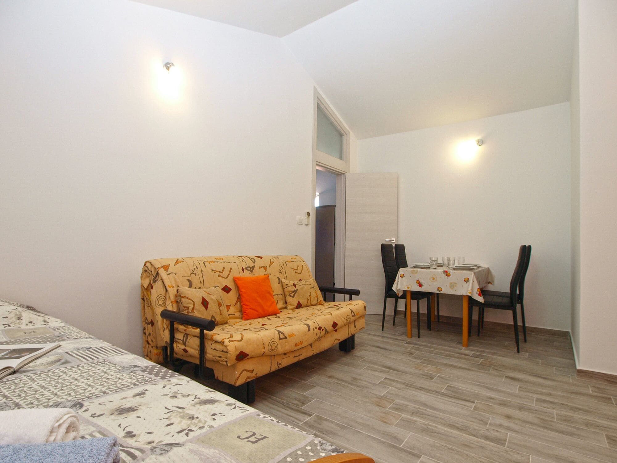 Una habitación pequeña y bien iluminada con un sofá, una mesa de comedor con sillas y una cama.