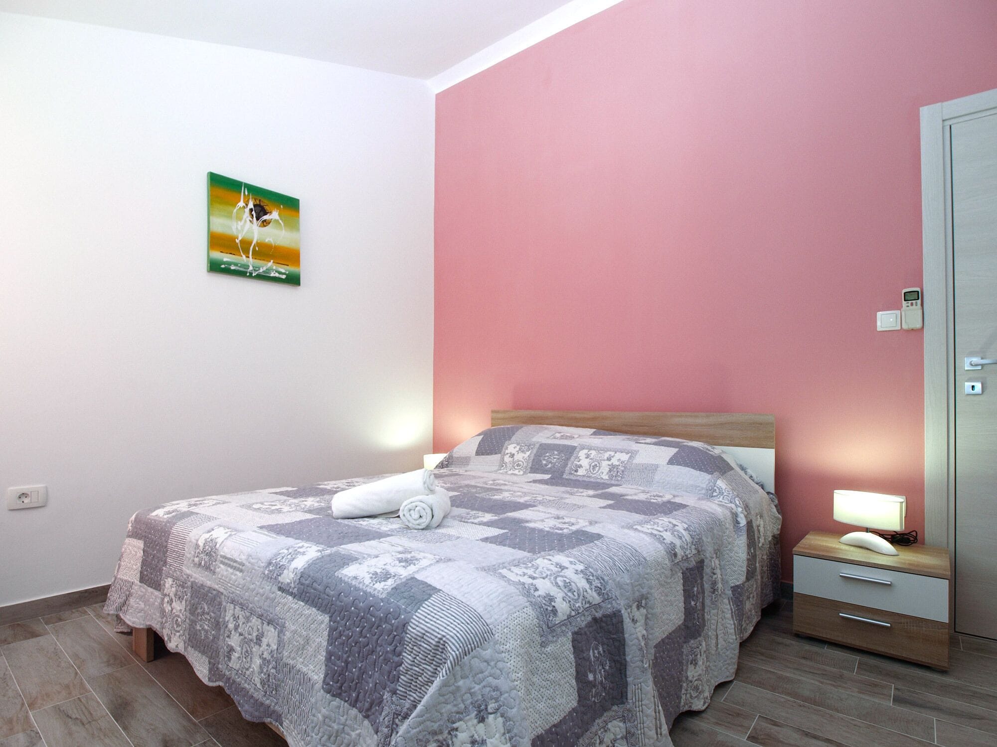 Un dormitorio con cama, mesita de noche, luz de pared e interruptor.