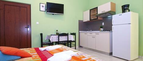 A small, well-lit bedroom with a bed, a bedside table, and a television mounted on the wall.