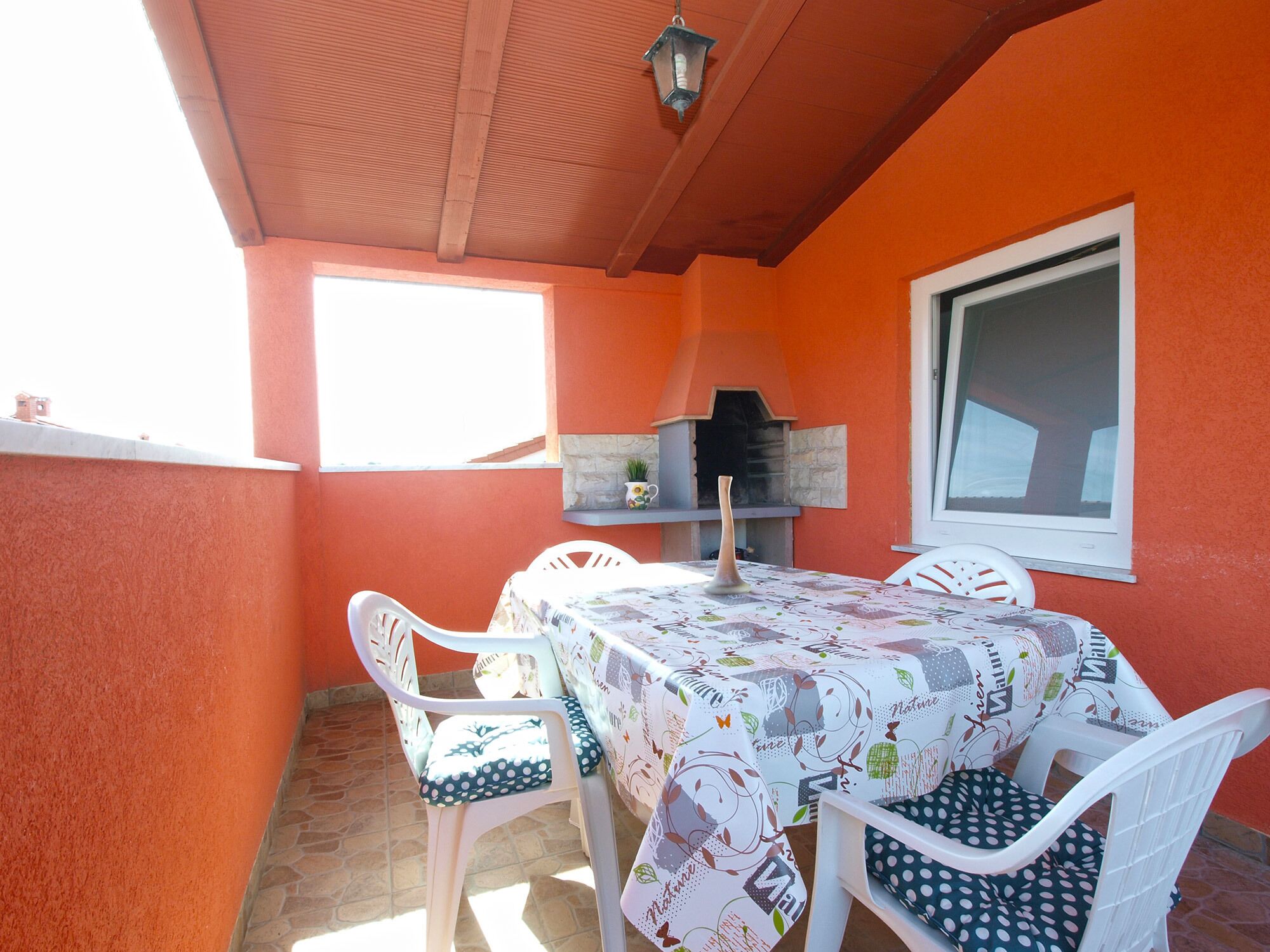 Une terrasse extérieure avec une table et des chaises, un four à pizza et une fenêtre.