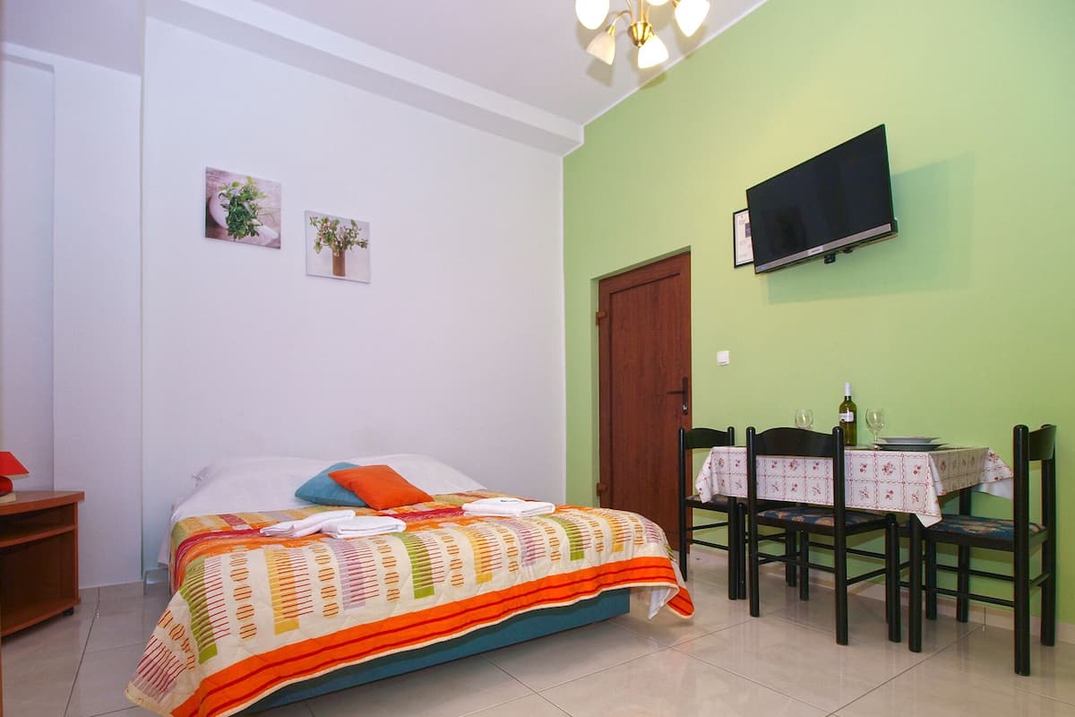 Ein Schlafzimmer mit Bett, Wandfernseher, Esstisch mit Stühlen und einer Tür.