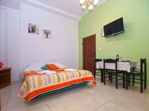 Une chambre à coucher avec un lit, un téléviseur fixé au mur, une table à manger avec des chaises et une porte.