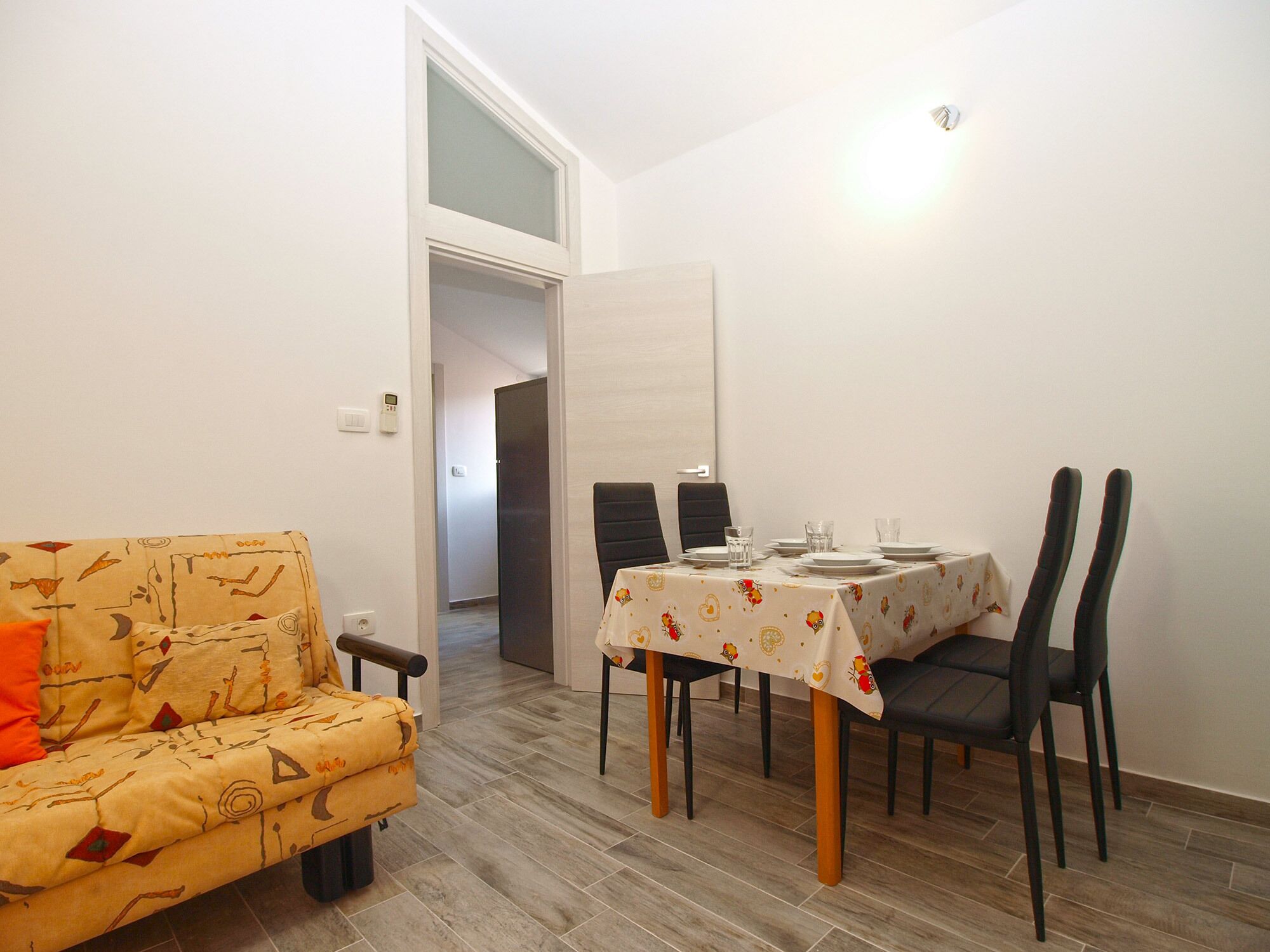 Un comedor con una mesa dispuesta para cuatro personas, un sofá y una puerta que da a otra habitación.