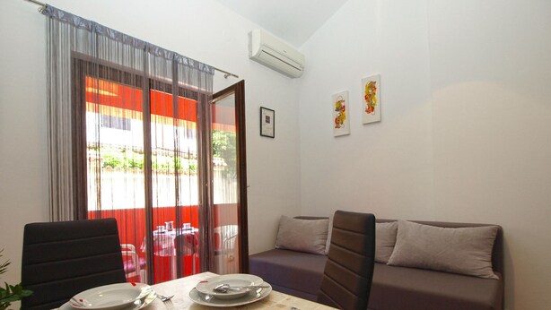 A dining area with a table set for two, a sofa, and a sliding glass door leading to an outdoor area. - Apartments Orijana 898 (Pula)