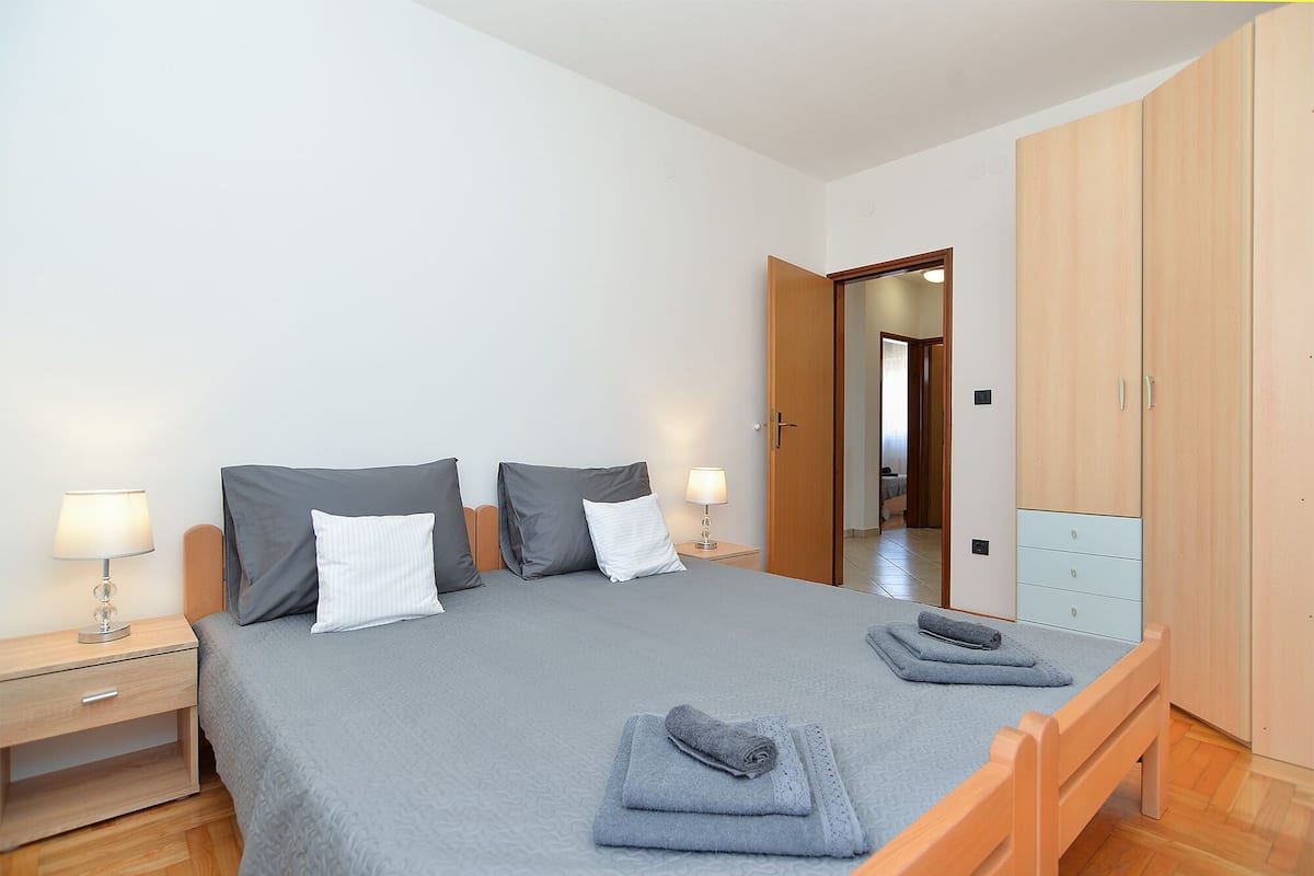 A neatly made bed with grey bedding, two bedside lamps, and a wooden wardrobe.