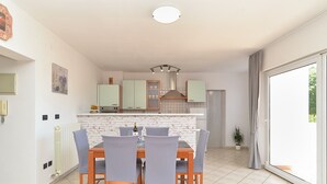 A compact kitchen with a dining area, featuring a white brick backsplash, light green cabinets, and a central island. - Apartments Emil 596 (Pula)
