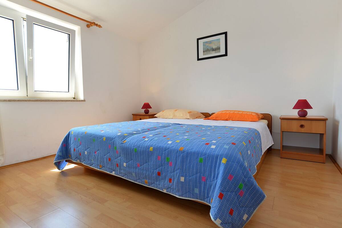 A bedroom with a bed, two bedside tables, a window, and a picture on the wall.