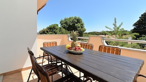 A balcony with a wooden table and chairs, a bowl of fruit, and a view of trees and buildings. - Apartments Emil 596 (Pula)