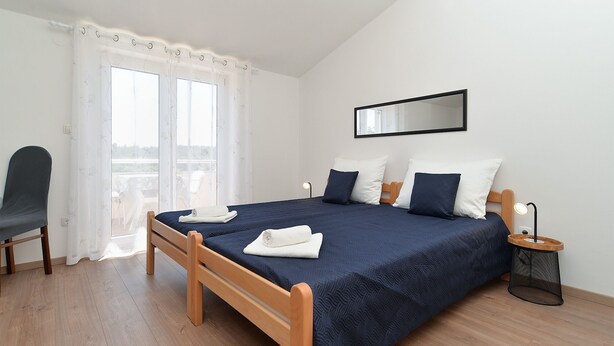 A bedroom with a bed, a chair, a bedside table, a lamp, and a window with curtains. - Apartments Emil 596 (Pula)