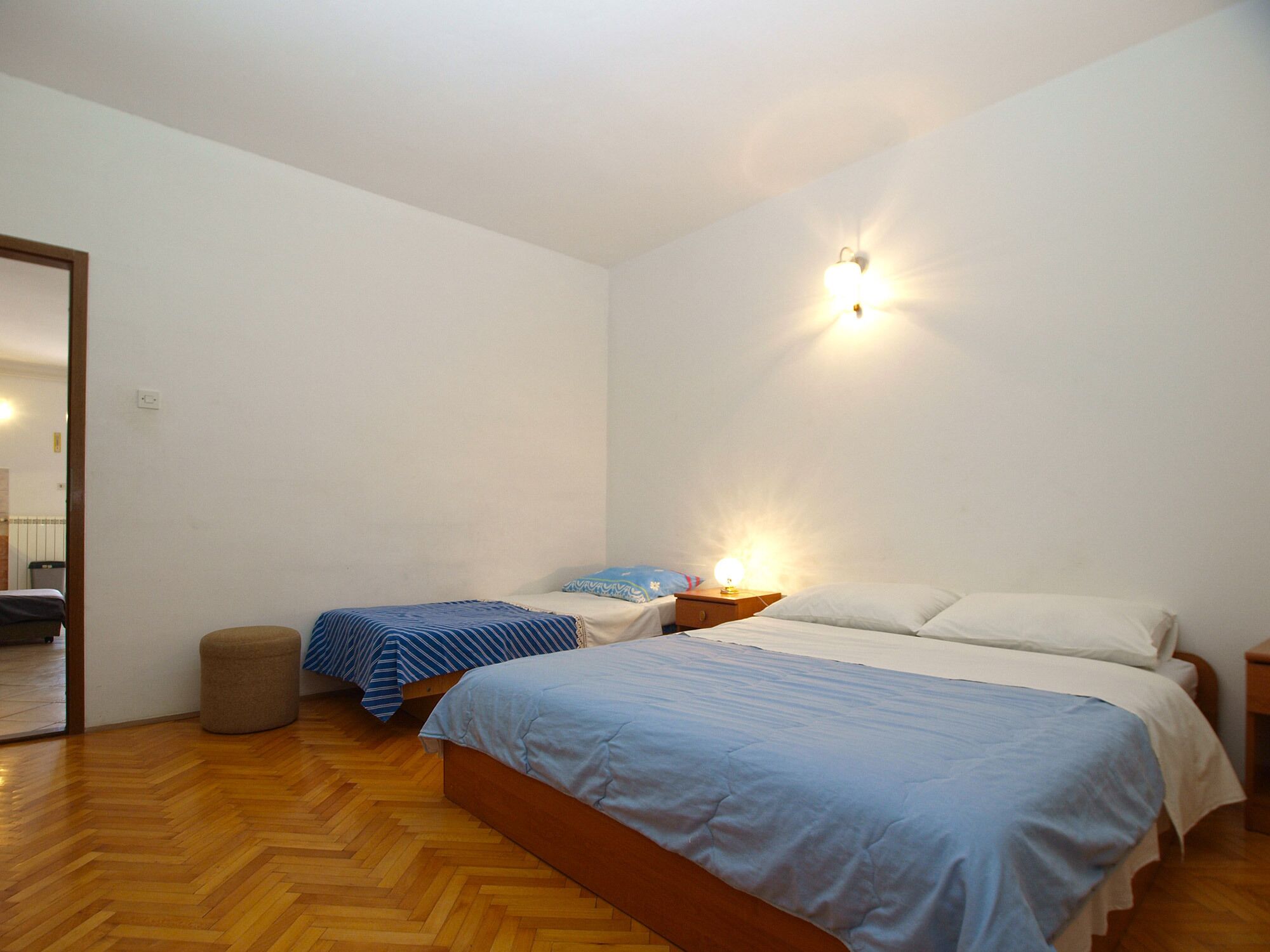 Une chambre avec deux lits, un plancher en bois et une table de chevet avec une lampe.