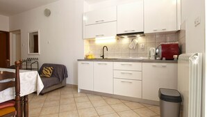 Een kleine keuken met witte kastjes, een spoelbak en een rode waterkoker.