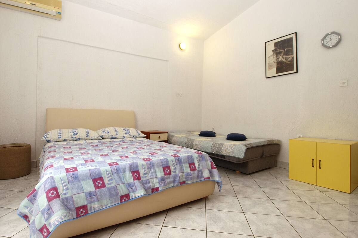 A bedroom with a bed, a nightstand, a small sofa, a yellow cabinet, and a wall clock.
