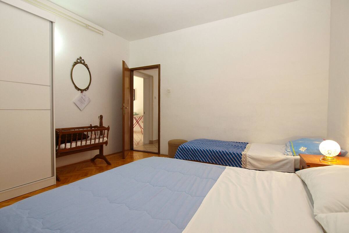 A bedroom with a large bed, a smaller bed, a wooden chair, a mirror, and a door leading to another room.