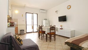 Een knus woongedeelte met kitchenette, een eethoek met tafel en stoelen, een bed, een televisie en een glazen schuifdeur naar een buitenruimte.