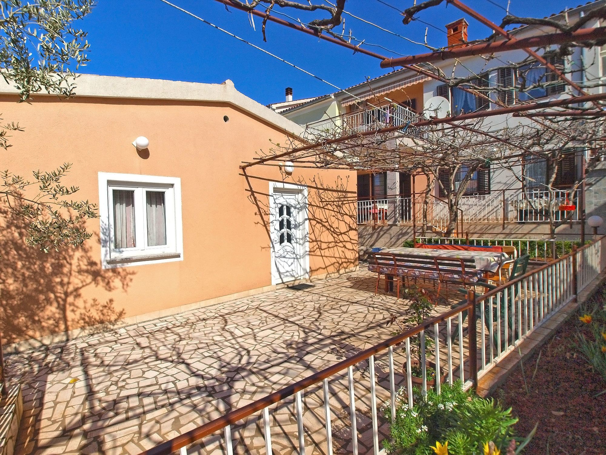 A courtyard with a tiled floor, a pergola, and a small table with chairs.