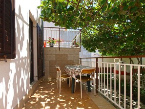 Un pequeño patio exterior con una mesa y sillas, rodeado por una cerca blanca y una planta en maceta.