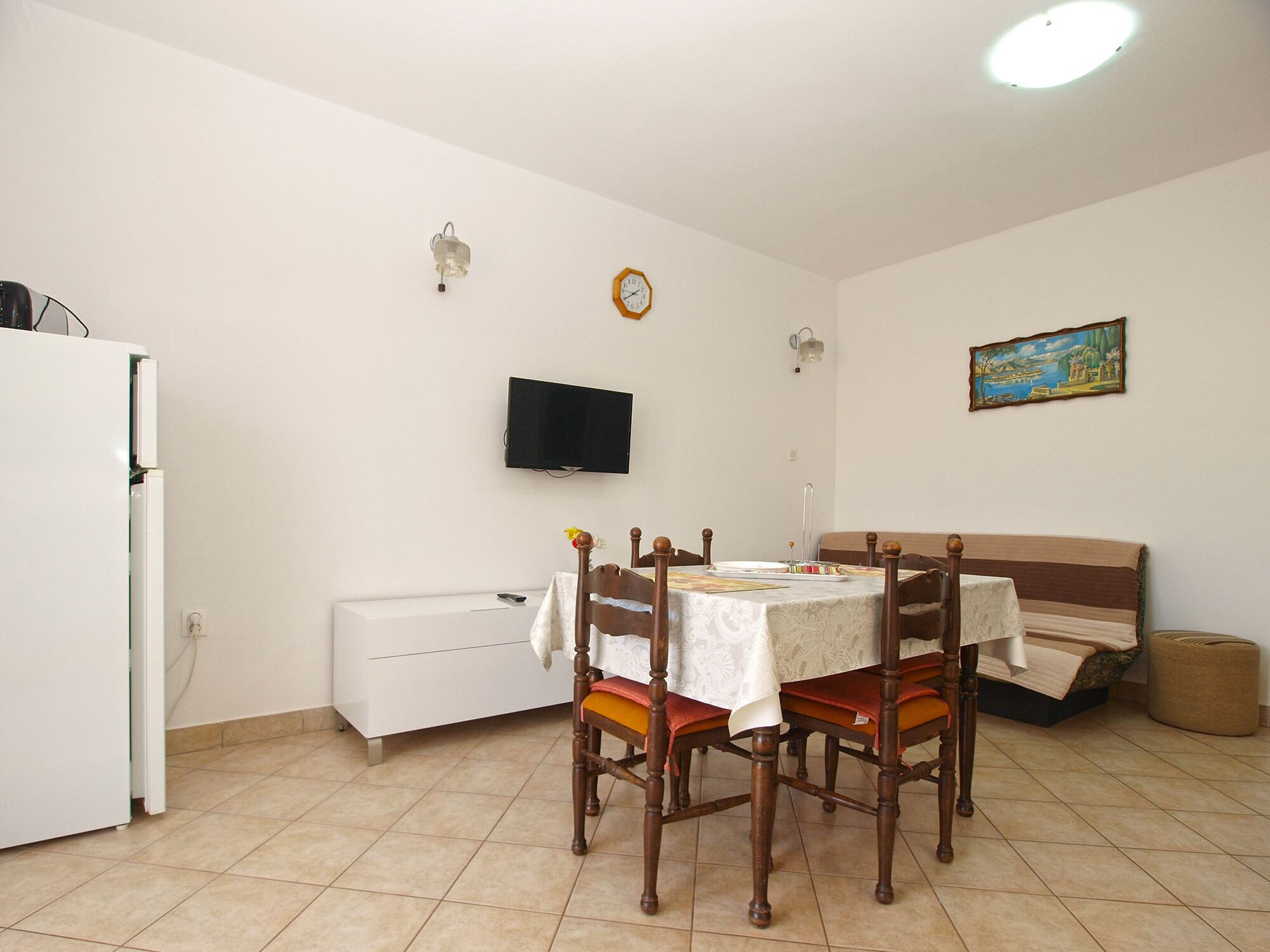 A small, clean room with a dining table, chairs, a sofa, a TV, and a painting on the wall.