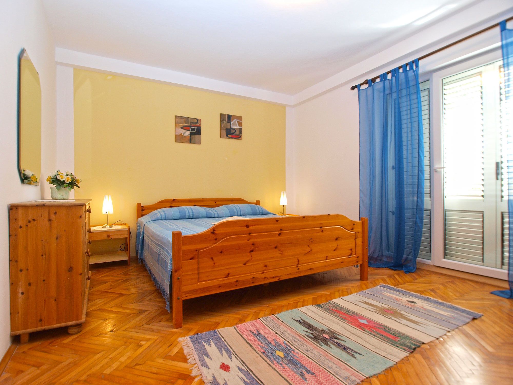 A bedroom with a wooden bed, a nightstand, a dresser, and a window with blue curtains.
