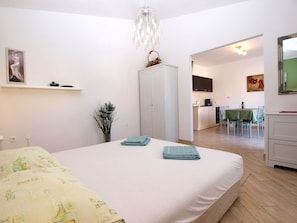 Un dormitorio con cama, mesita de noche, cómoda, espejo y vista a la cocina.