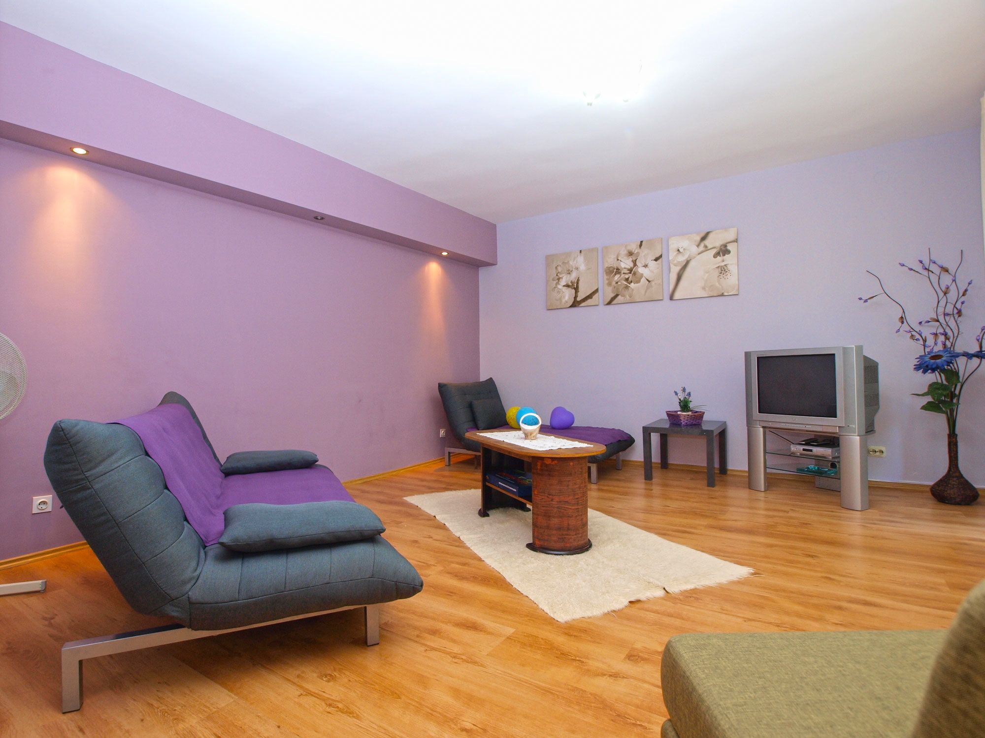 A living room with a sofa, a small table, a television, and a vase with flowers.