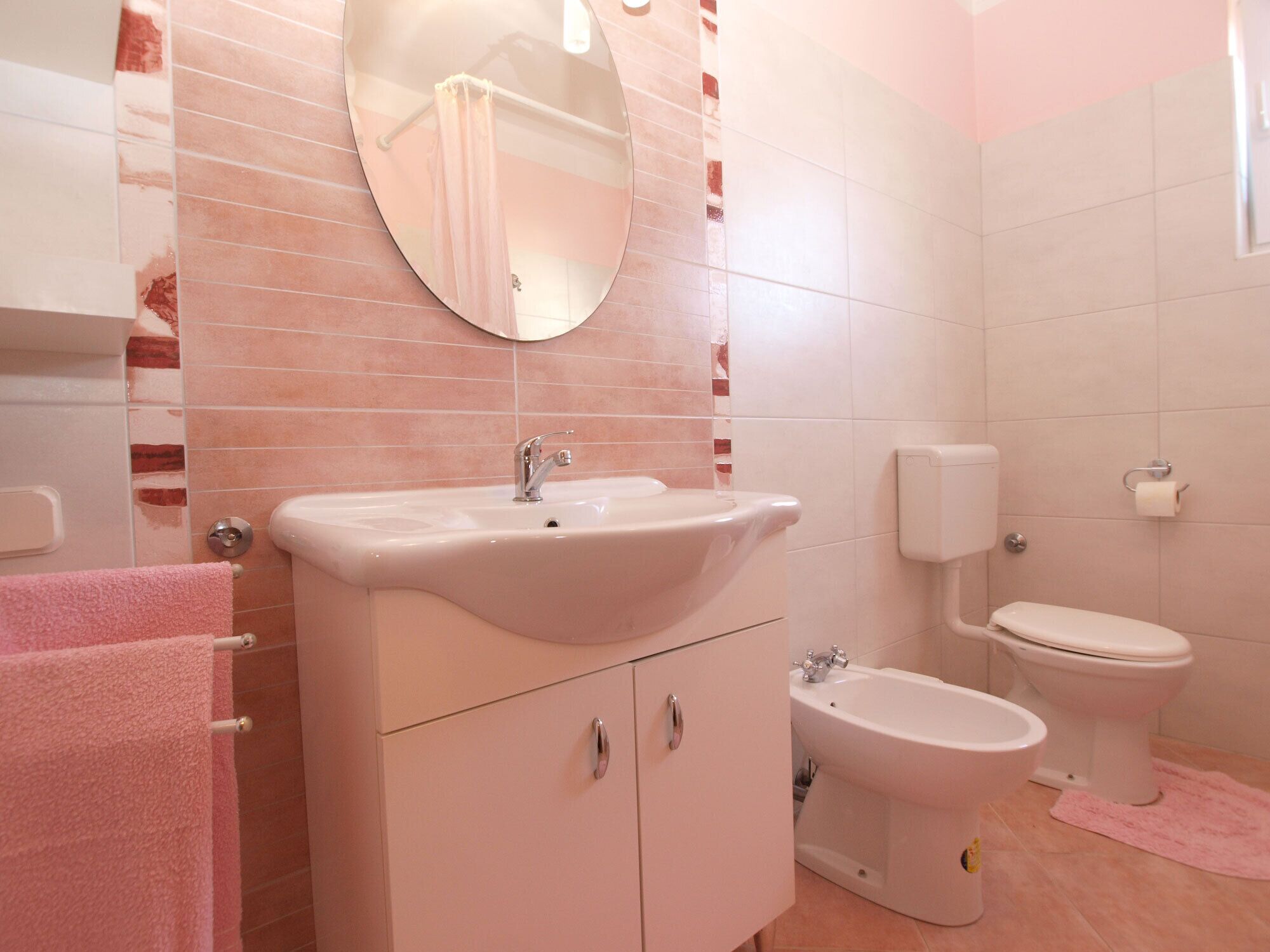 Ein Badezimmer mit Waschbecken, Spiegel, Toilette, Bidet und rosa Handtüchern.