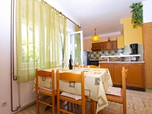 Un comedor con una mesa dispuesta para cuatro, una cocina al fondo y una ventana con cortinas translúcidas.