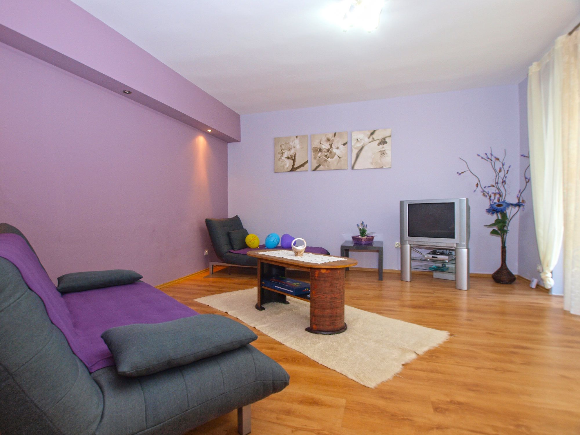 A living room with a sofa, a coffee table, a TV, and a vase with flowers.
