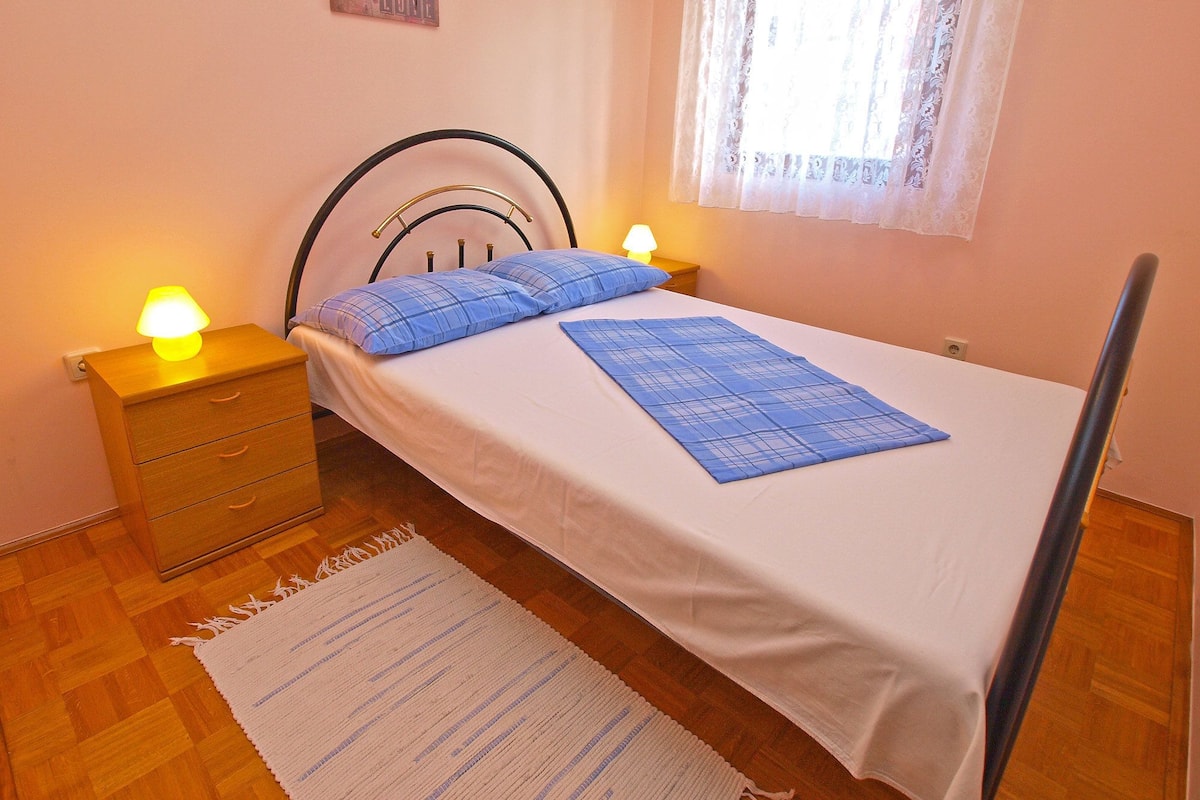 Une chambre à coucher comprenant un lit, deux tables de chevet, une commode, une horloge murale, une fenêtre avec des rideaux en dentelle et une lampe sur pied.