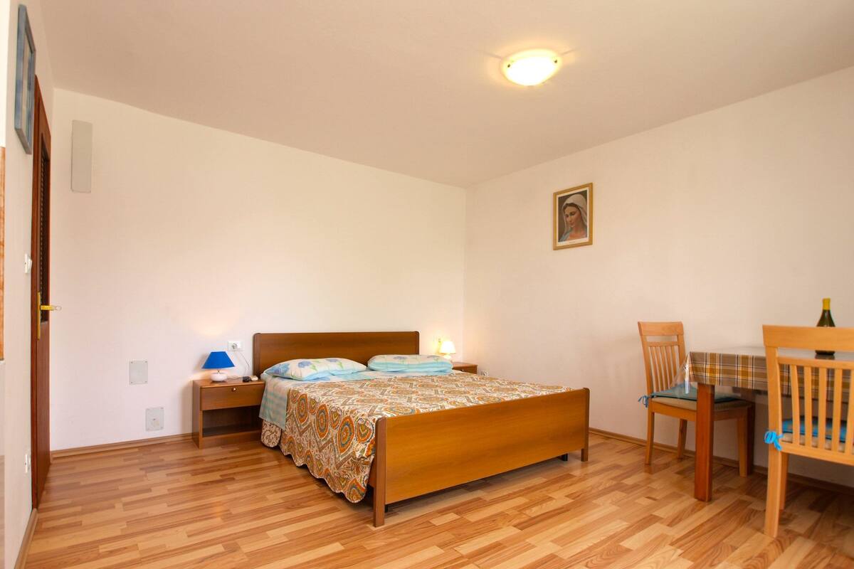 Quarto com cama de madeira, mesa de cabeceira, cadeira, mesa e luminária no teto.