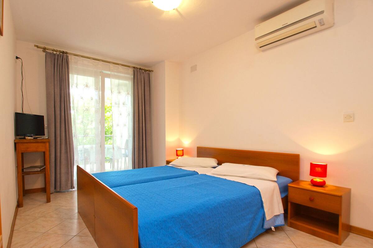 Quarto de hotel com cama, duas mesas de cabeceira, televisão e ar condicionado.