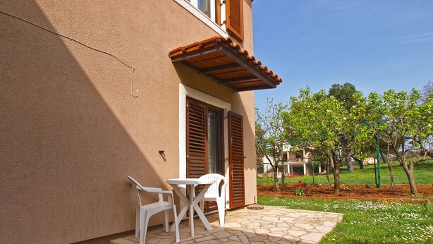 A building with a stone patio, white plastic chairs, and a small table. - Apartments Marta 1066 (Rovinj)