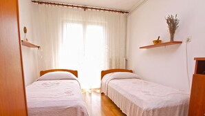 A room with two single beds, wooden flooring, a window with curtains, and a shelf with a vase. - Apartments Marta 1066 (Rovinj)