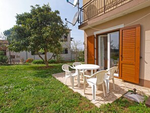 A patio with a table and chairs, a tree, and a building with a balcony. - Apartments Marta 1066 (Rovinj)