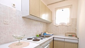 A compact kitchen with a gas stove, oven, and a small sink. There is a window above the sink, and the walls are tiled. - Apartments Marta 1066 (Rovinj)